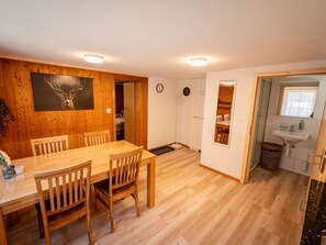Ein Essbereich mit Holztisch und Stühlen, einer Uhr an der Wand und Blick in eine Küche mit Spüle und Fenster.