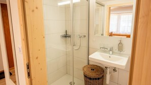 Kylpyhuone, jossa on lasiseinäinen suihkukaappi, valkoinen pesuallas ja rottinkikori.