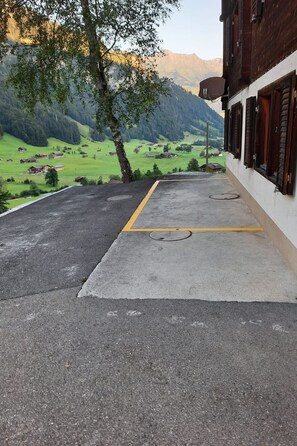 Uma área pavimentada com uma linha amarela, uma árvore e um prédio com persianas de madeira.