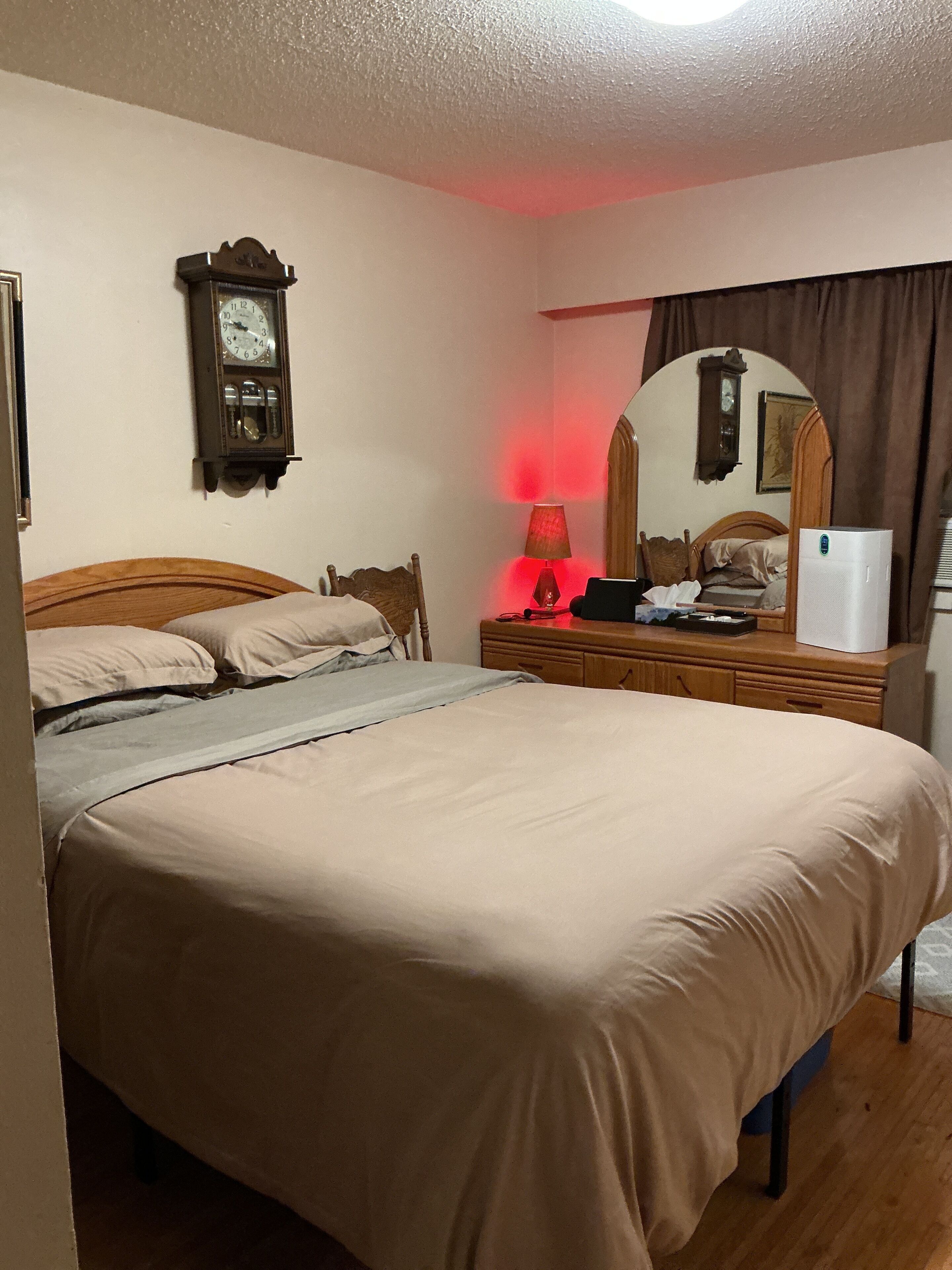 Un dormitorio con cama, mesita de noche, lámpara, espejo y un reloj de pared.