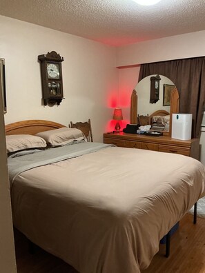 A bedroom with a bed, a nightstand, a lamp, a mirror, and a wall clock. -     •     Cozy 1-Bedroom Retreat | Private & Comfortable Stay (Delta)