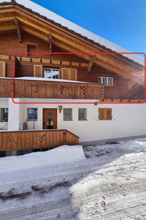 Eine zweistöckige Holzchalet mit Balkon, schneebedecktem Grund und blauem Himmel.