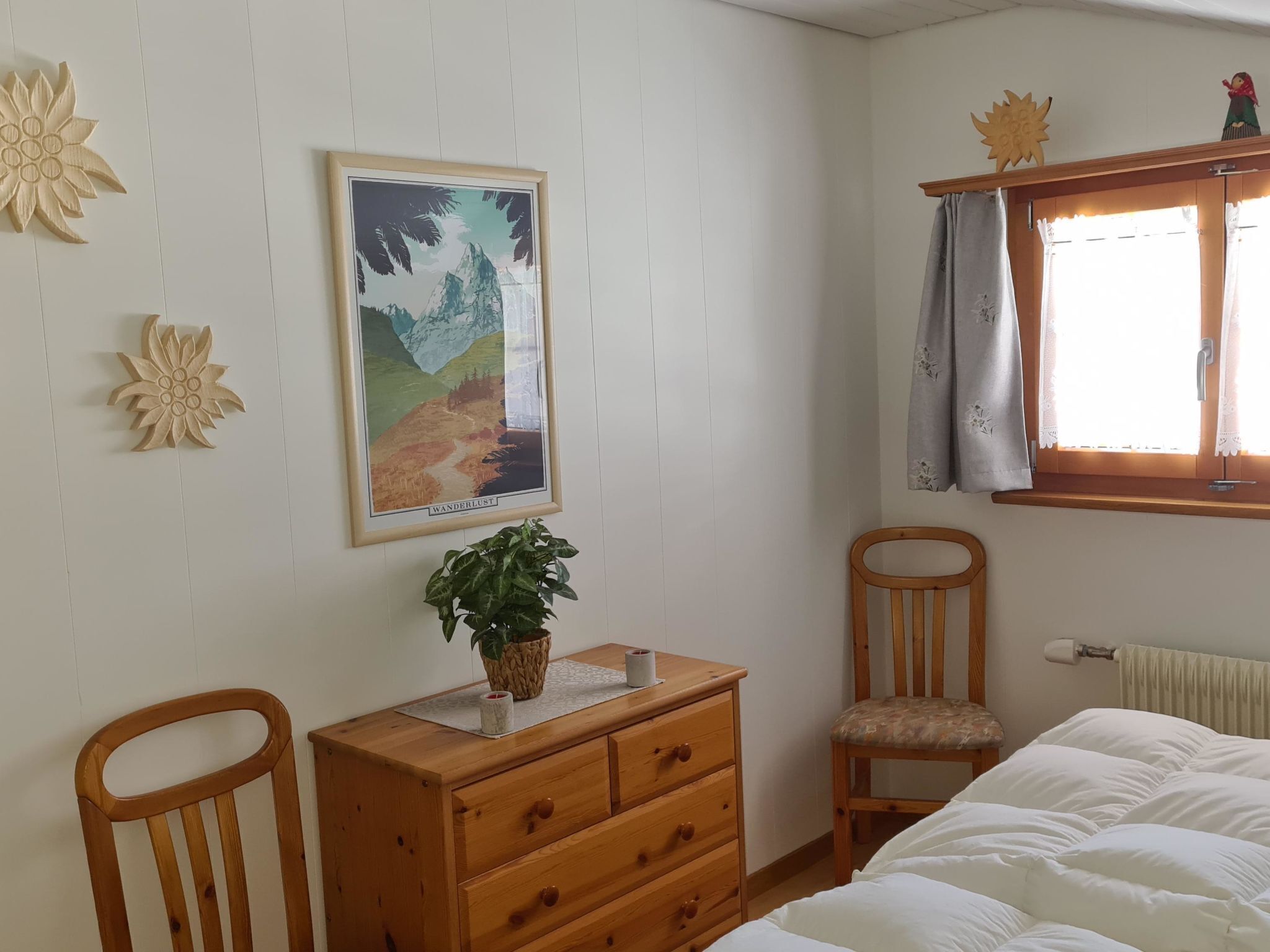 Een slaapkamer met een bed, een houten dressoir, een stoel, een raam met gordijnen en een poster op de muur.