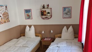 Ett rum med två enkelsängar, ett litet nattduksbord med en lampa och en hylla med böcker och prydnadsföremål.