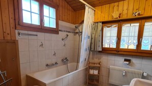 Ett badrum med badkar, toalett, dusch och ett fönster med gardiner.