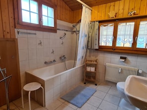 Ein Badezimmer mit Badewanne, Toilette, Dusche und einem Fenster mit Vorhängen.