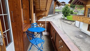 En balkong i trä med ett bord och några stolar, med utsikt över en bostadsgata.