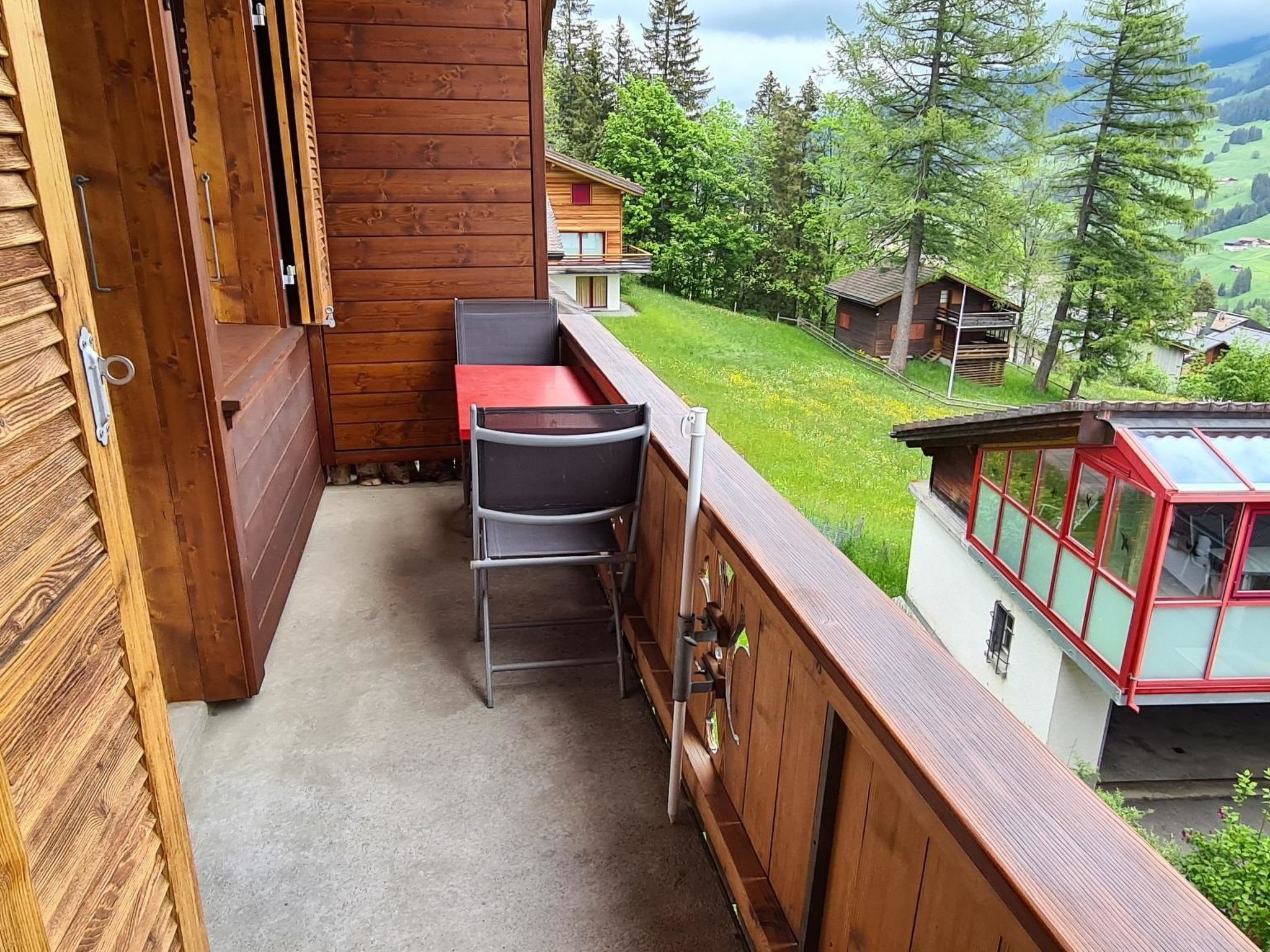 Un balcón de madera con una mesa y sillas, con vistas a un paisaje verde con casas.