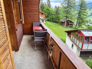Un balcón de madera con una mesa y sillas, con vistas a un paisaje verde con casas.