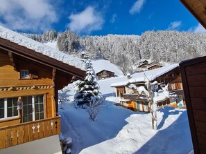 Eine Holzhütte mit schneebedecktem Dach, umgeben von verschneiter Landschaft und blauem Himmel.