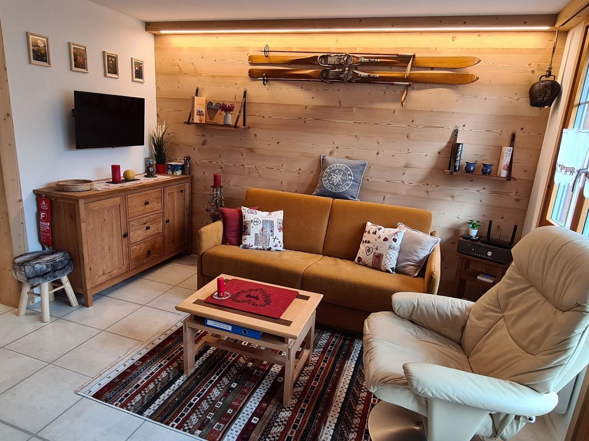 Un salón acogedor con sofá, sillón, aparador de madera y esquíes en la pared.