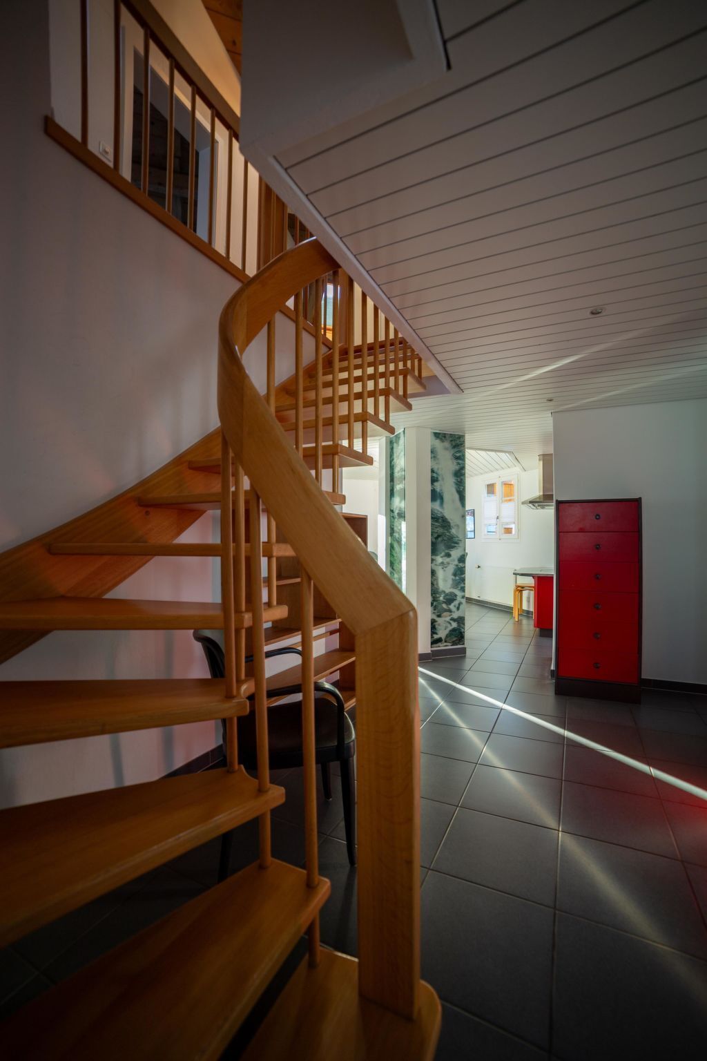 A wooden staircase leading to a room with a tiled floor and a red cabinet.