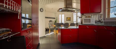 A modern kitchen with red cabinets, a microwave, and a dining area with chairs and a table.