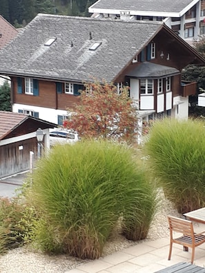 A residential building with a sloped roof, a visible chimney, and a small garden area with trimmed bushes. - Surselva Appartement/Fewo, Dusche, WC, Balkon 6-Zimmerwohnung by Interhome (Adelboden)