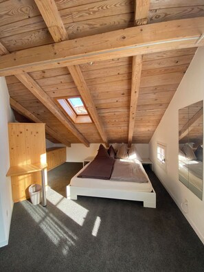 A bedroom with a sloped ceiling, a skylight, a bed with pillows, a small bedside table, and a mirror on the wall. - Surselva Appartement/Fewo, Dusche, WC, Balkon 6-Zimmerwohnung by Interhome (Adelboden)