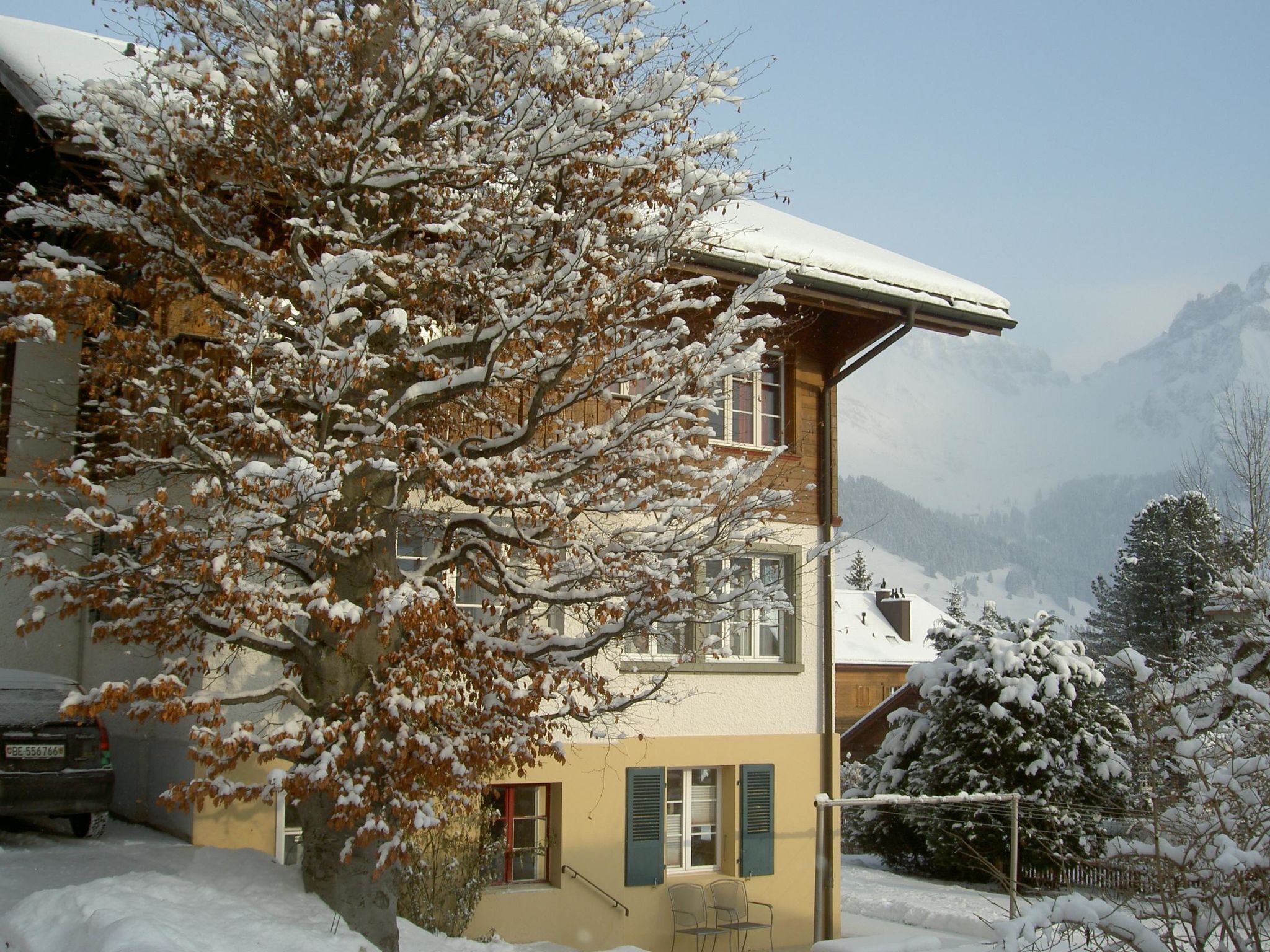 Un edificio de dos pisos con tejado nevado y un árbol grande al frente.