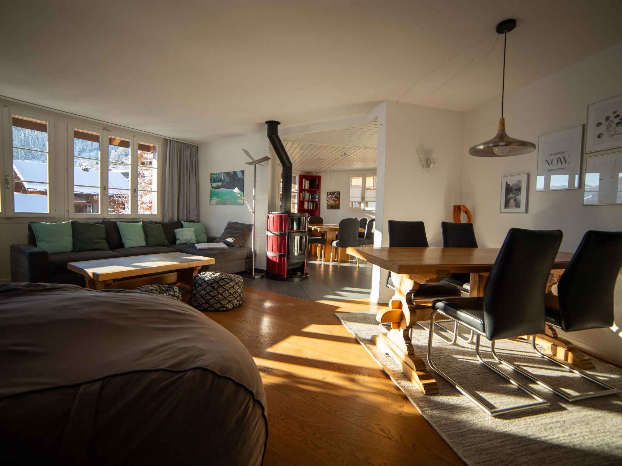 En moderne stue med sofa, spisebord og stole. Der er pejs, reol og et vindue med udsigt over et sneklædt landskab.