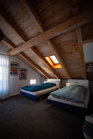 Ein Zimmer mit schrägem Dach, zwei Betten, einem Oberlicht und einem Fenster.