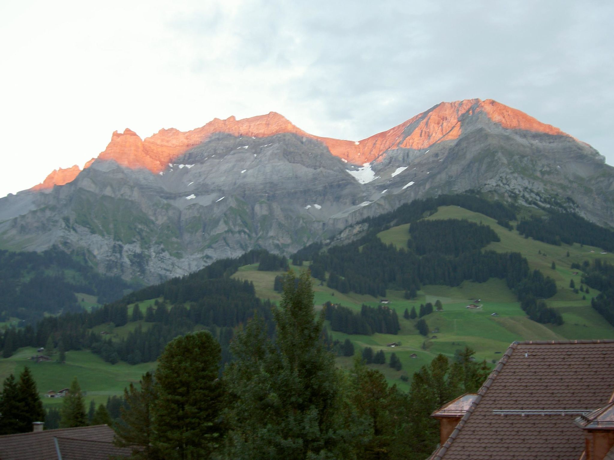 A mountain range with a prominent peak, forested valleys, and a residential area with houses.