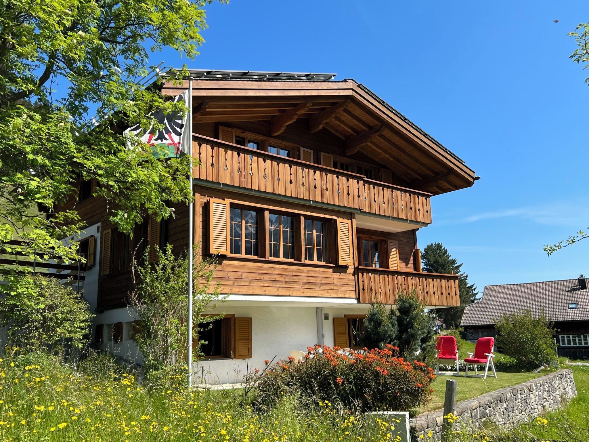 Eine zweistöckige Holzhütte mit Balkonen, umgeben von Grünpflanzen und Blumen.