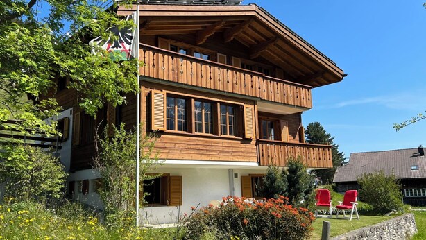 A two-story wooden chalet with balconies, surrounded by greenery and flowers. - Im Rägeboge Appartement/Fewo, Bad, WC, 2 Schlafräume 3-Zimmerwohnung Dachstock by Interhome (Adelboden)