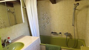 A bathroom with a green bathtub, a sink with a mirror, and a toilet. - Im Rägeboge Appartement/Fewo, Bad, WC, 2 Schlafräume 3-Zimmerwohnung Dachstock by Interhome (Adelboden)