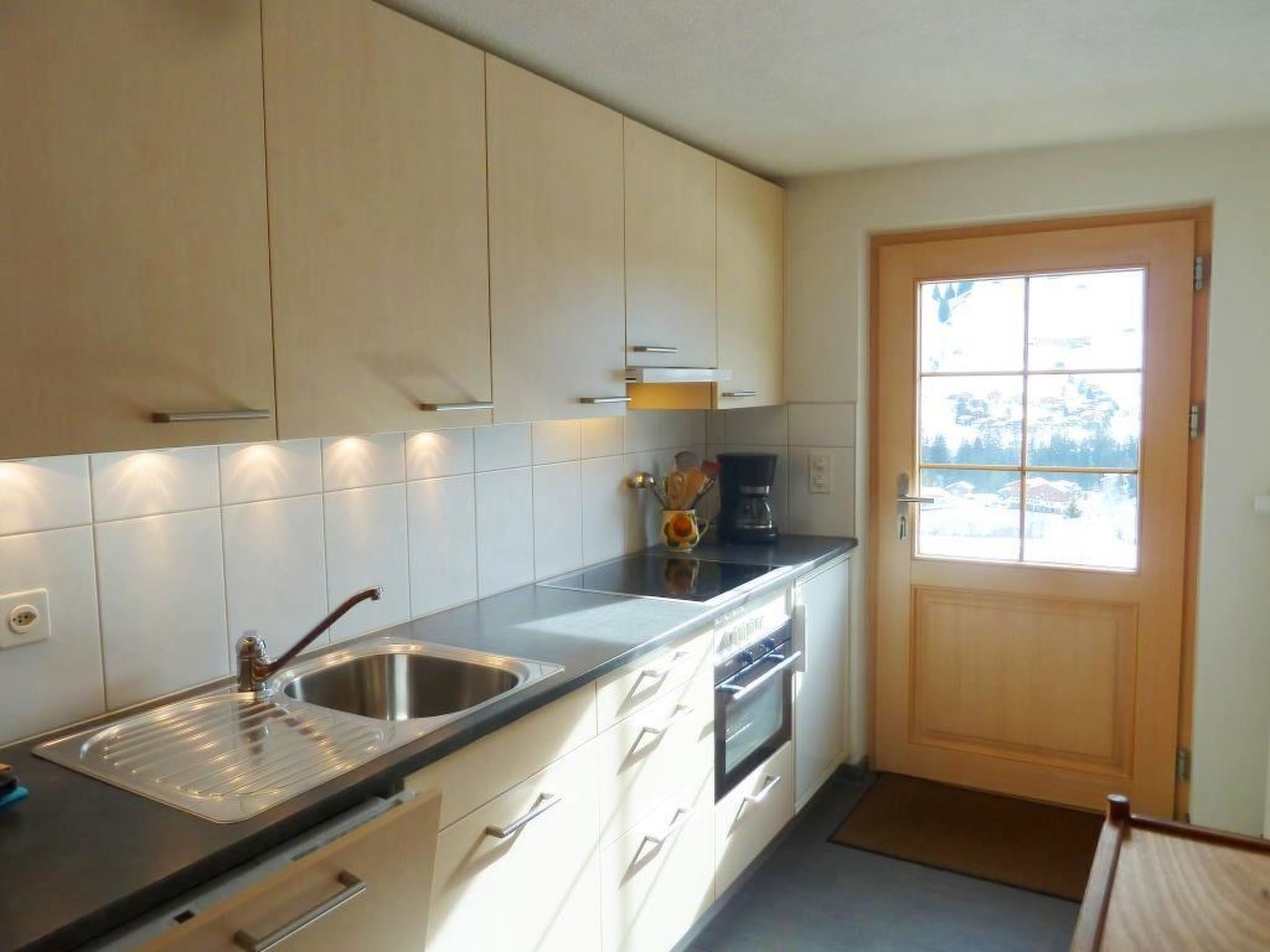 Une cuisine moderne avec des meubles blancs, un évier en acier inoxydable et une porte en bois.