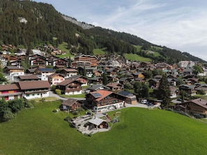 Ein Bergdorf mit traditionellen Holzhäusern, ein zentrales Gebäude mit geneigtem Dach und einem Spielplatz.