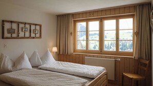 A room with two beds, a wooden chair, a window with curtains, and a radiator. - Gästehaus Alpengruss Appartement/Fewo, Dusche, WC, 1 Schlafraum by Interhome (Adelboden)
