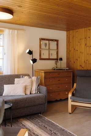 A cozy living room with a sofa, a chair, a wooden dresser, and a wall-mounted mirror. - Gästehaus Alpengruss Appartement/Fewo, Dusche, WC, 1 Schlafraum by Interhome (Adelboden)