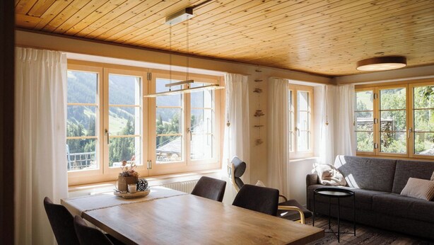 A spacious living area with a wooden dining table, black chairs, a sofa, and a view of the outdoors. - Gästehaus Alpengruss Appartement/Fewo, Dusche, WC, 1 Schlafraum by Interhome (Adelboden)