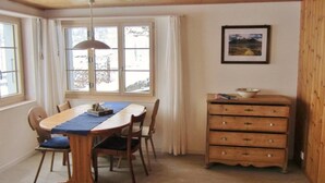 A dining area with a wooden table, chairs, a blue table runner, a pendant light, and a dresser with drawers. - Gästehaus Alpengruss Appartement/Fewo, Dusche, WC, 1 Schlafraum by Interhome (Adelboden)