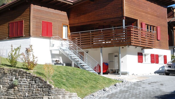 Ein zweistöckiges Holzhaus mit Balkon, Treppe und einer Steinmauer.
