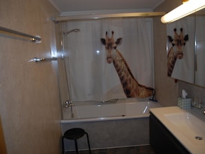Ett badrum med dusch, handfat och en spegel som reflekterar en giraff.