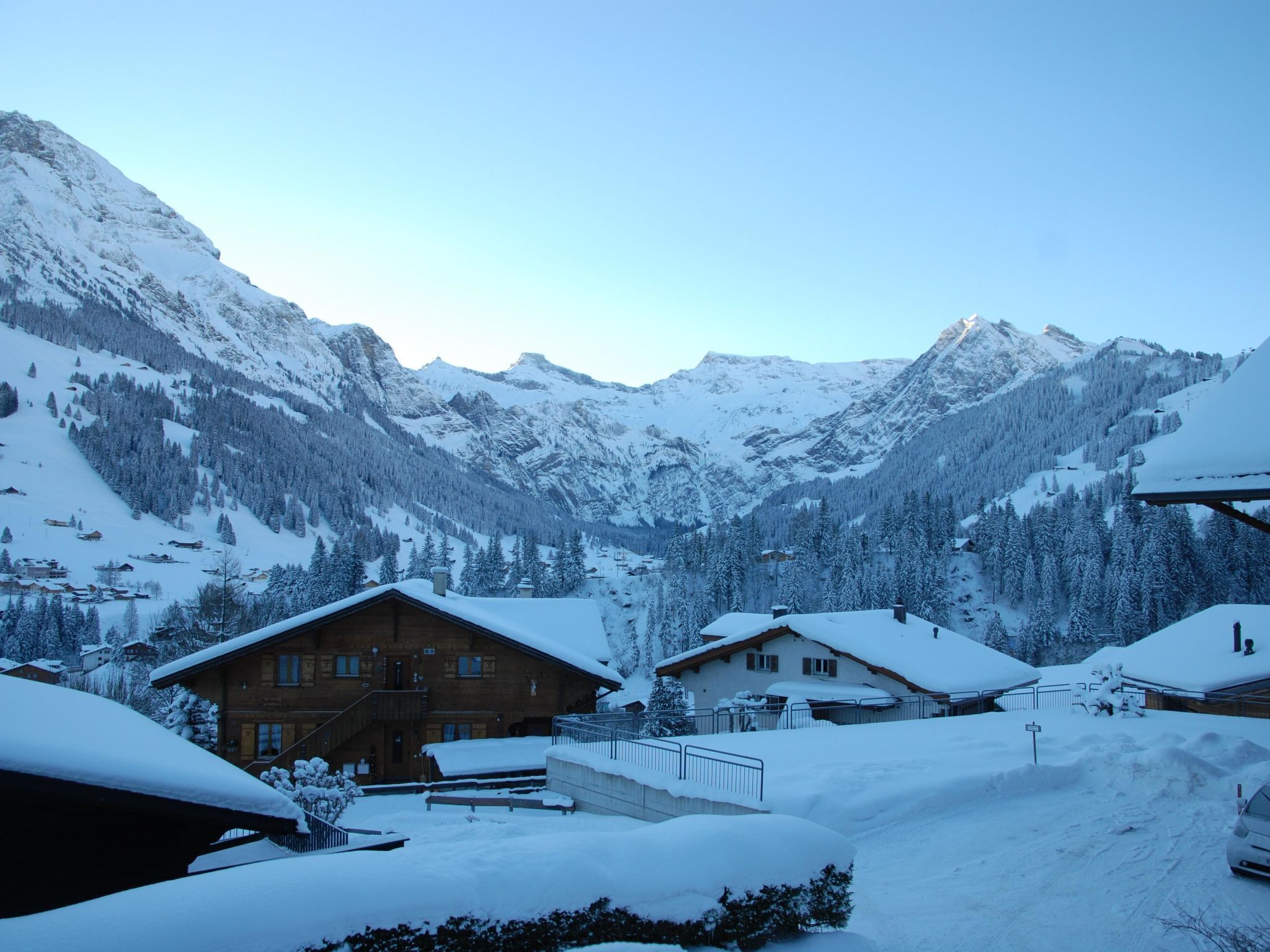 Un village de montagne enneigé, avec des maisons en bois et un ciel dégagé.