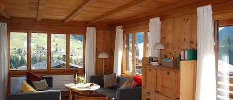 A wooden interior with a dining area, sofas, and a view of the outdoors.