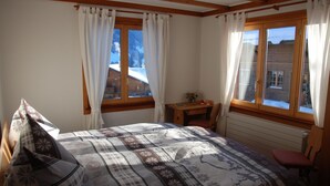 Ein Schlafzimmer mit einem Bett, einem kleinen Tisch, einem Stuhl und einem Fenster mit Blick auf eine verschneite Landschaft.