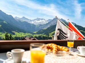 A breakfast table with croissants, juice, and coffee, overlooking a mountainous landscape with a flag. - Ravinel 2 Appartement/Fewo, Dusche, WC, 3 Schlafräume 4-Zimmerwohnung by Interhome (Adelboden)