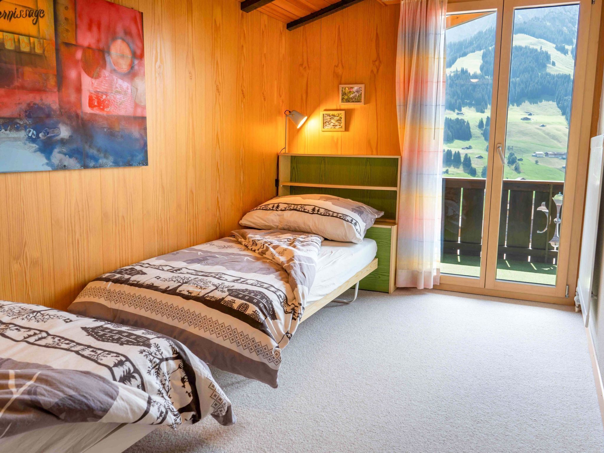 A bedroom with two single beds, a nightstand, a wall-mounted lamp, and a large window with a view of a mountainous landscape.