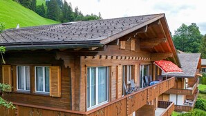 En flervånings chalet i trä med balkonger, stora fönster och ett sluttande tak.