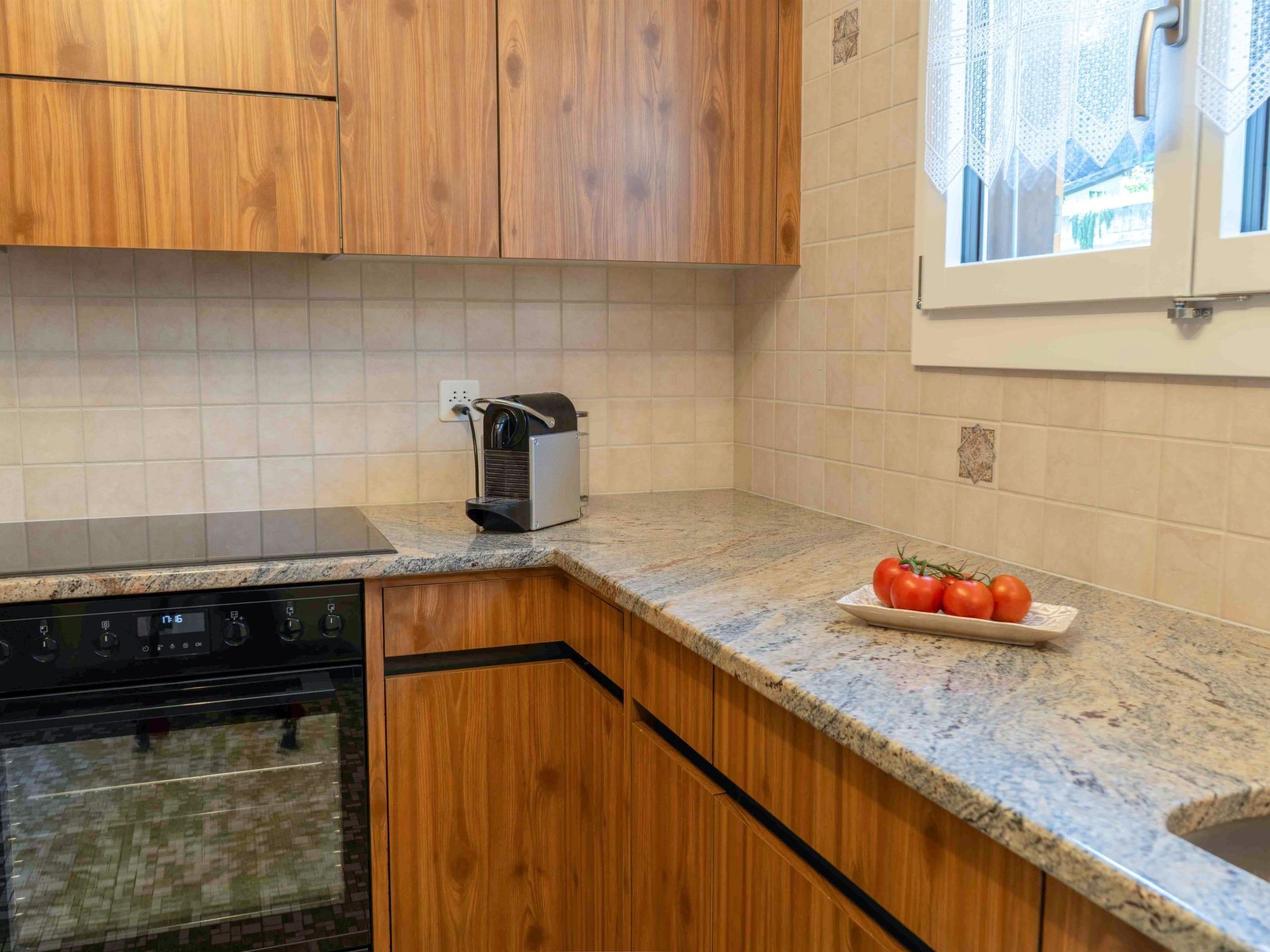 Una cocina con armarios de madera, horno integrado, microondas y una encimera con un plato de tomates.