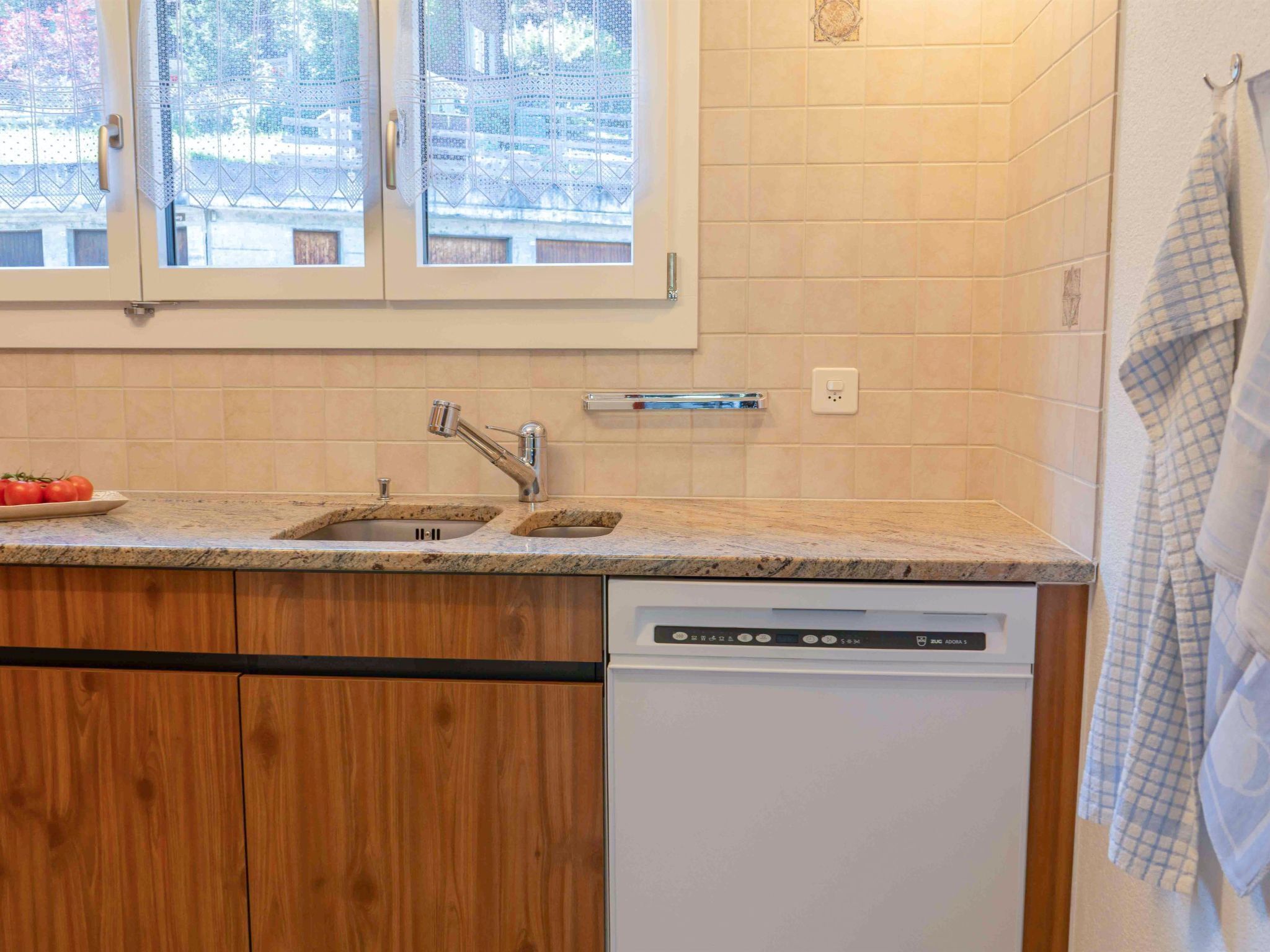 Una cocina con un lavamanos doble, armarios de madera, lavavajillas y una ventana con vistas a un edificio.