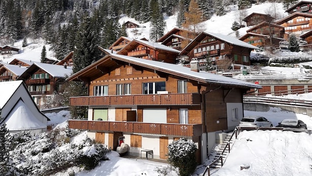 Ett hotell i chalet-stil med flera balkonger av trä, omgivet av snötäckta träd och berg.