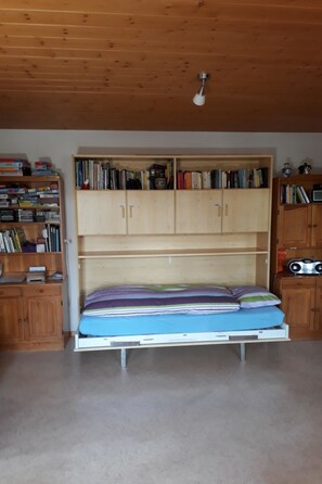 Ein Zimmer mit einem Bett, Holzregalen und einer Deckenleuchte.
