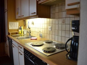 A kitchen with a stove, sink, and coffee maker. - Adlerhorst Appartement/Fewo, Dusche, WC, 2 Schlafräume 3-Zimmerwohnung by Interhome (Adelboden)