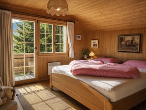 Ein Schlafzimmer mit Holzwandverkleidung, einem großen Bett, einem Heizkörper und Blick auf Grün hinter den Fenstern.