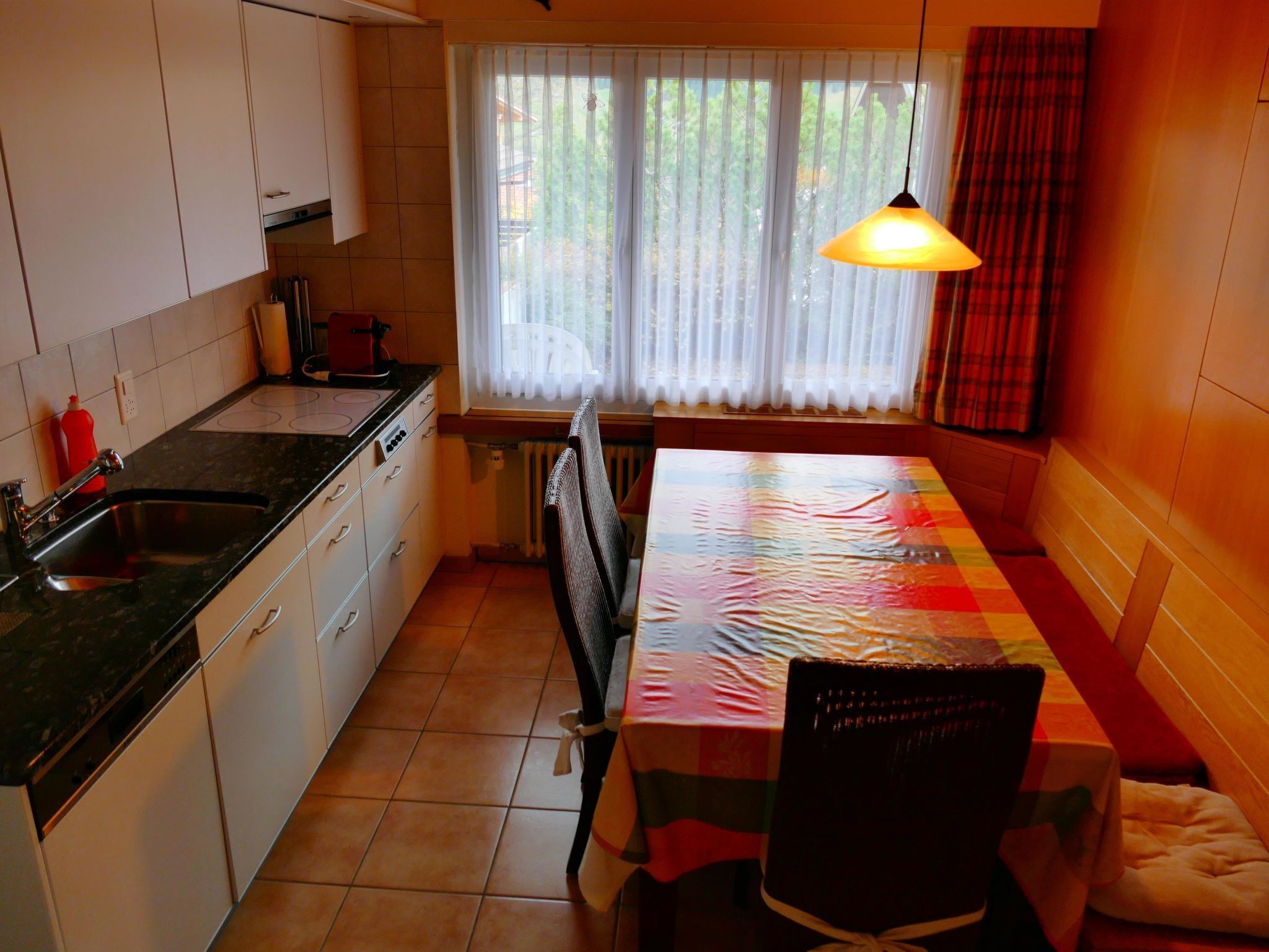A kitchen with a dining area, a window with curtains, and a hanging light fixture.
