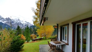 A patio area with a table and chairs, a small garden with grass and shrubs, and a view of mountains in the background. - Silberdistel  B09 Appartement/Fewo, Bad, WC, 3 Schlafräume 3.5 Zimmerwohnung by Interhome (Adelboden)