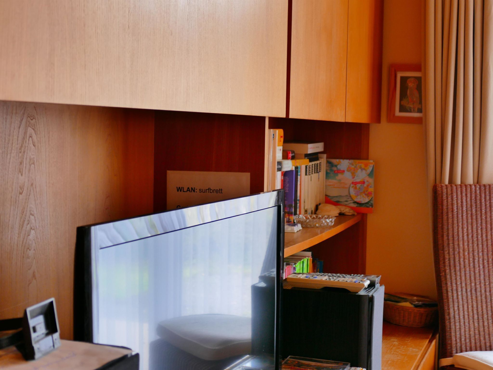 Ein Zimmer mit Schreibtisch, Bücherregal und einem Schild mit der Aufschrift 'WLAN: surfbrett'.