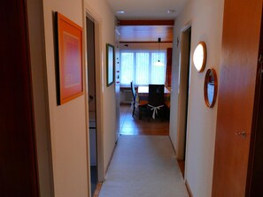 Corredor que dá para uma sala de jantar com mesa e cadeiras, um radiador e uma janela com cortinas.